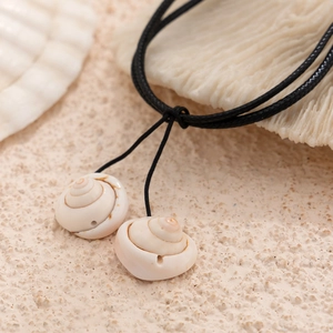 Detail of natural conch shells on black cord against a sandy coastal background