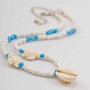 Detail of seashell and sea turtle pendants on blue beaded necklace with silver clasp