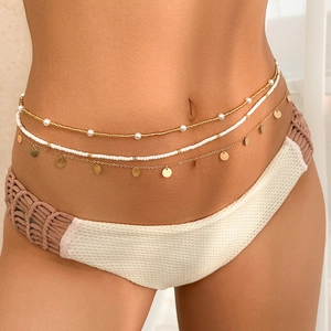 Detail of layered waist chain featuring gold sequins, white beads and pearls on skin