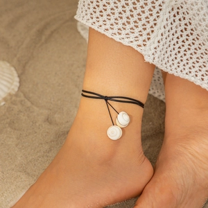 Detailed view of beach shell anklet with black cords and sea snail charms on sand