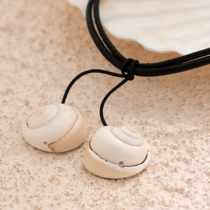 Macro shot of natural spiral conch shell pendants on black braided cord against sand