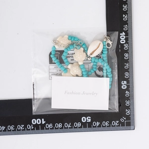 Detail of beach style turquoise beaded necklace with turtle and shell charms in packaging