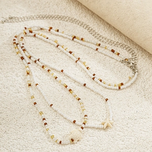 Détail de la chaîne de taille perlée avec pendentifs étoile de mer et tortue sur sable