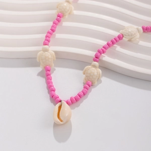 Detail of pink beaded necklace with sea turtle charms and a white cowrie shell pendant