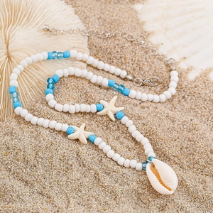 Detail of beach necklace featuring white starfish beads and natural shell on sand