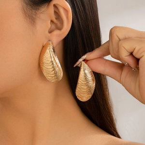 Primer plano de pendientes de gota dorados con textura acanalada en modelo mujer