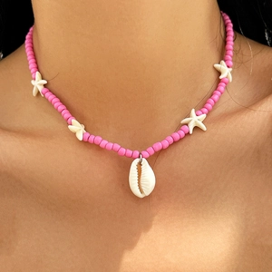 Detail of pink beaded beach necklace featuring white star charms and a natural seashell pendant