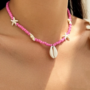 Detail of pink beaded necklace with white starfish and seashell charm on model