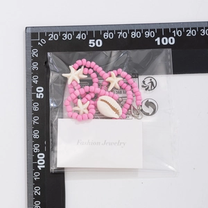 Detail view of pink beaded ocean necklace with starfish and shell charms next to a ruler