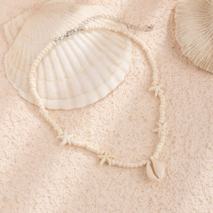 Detail of beaded starfish necklace with shell pendant on beach sand background
