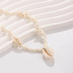 Macro detail of ocean themed beaded necklace featuring a natural conch shell and starfish