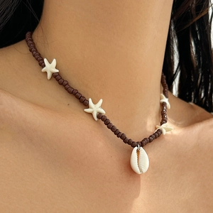 Detailed shot of a beach necklace with red seed beads, white starfish, and a natural cowrie shell