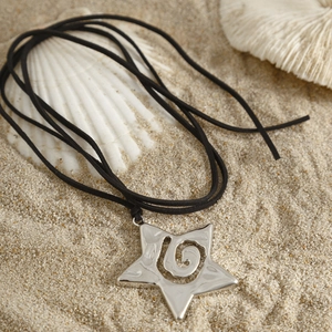 Primer plano de colgante de estrella de mar pulida con diseño en espiral en playa de arena y conchas