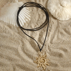 Collar con colgante de sol dorado y diseño en espiral sobre fondo de playa de arena