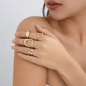 Nahaufnahme einer Hand mit vier unregelmäßigen Goldringen in minimalistischem Design