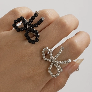 Macro detail of bead-strung bow rings in black and silver finishes on a grey background