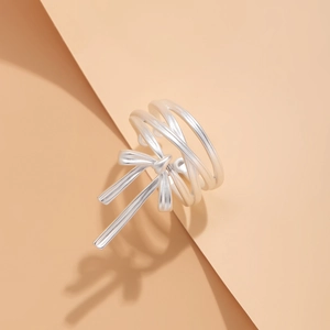 Detail of silver ribbon bow ring with layered crossover band on a warm beige background