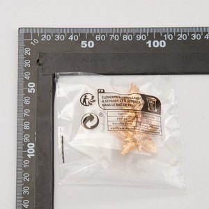 Close-up of golden metal leaf stud earring with brushed texture shown next to a ruler