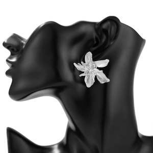 Close-up of large silver flower earrings with brushed metal petals on a black model