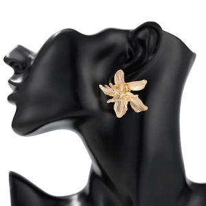 Detailed view of golden flower earrings with brushed metal texture on a black model stand