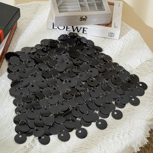 Macro shot of black sequins linked by silver rings on a sleek body chain skirt