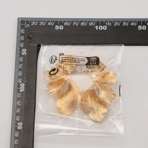 Detailweergave van grote gouden blad oorbellen met textuur en schaalverdeling voor maat