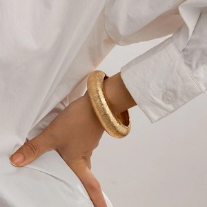Detail van een gouden brede gestructureerde armband met parels op een witte mouw