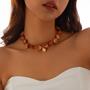 Detail of bohemian necklace with orange shell beads and gold pendant worn by a model