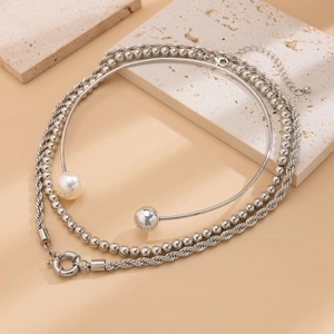 Macro detail of layered silver twist chain and rigid collar with white pearl and metal ball