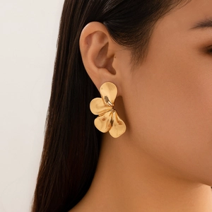 Close-up van een model met grote metallic gouden blad-oorbellen in een vintage bloemdessin