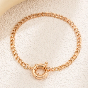 Detail of chunky gold curb chain bracelet featuring a large round spring nautical clasp