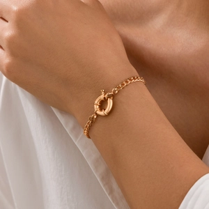 Detail of a chunky gold metal Cuban link bracelet with large bolt ring clasp on wrist