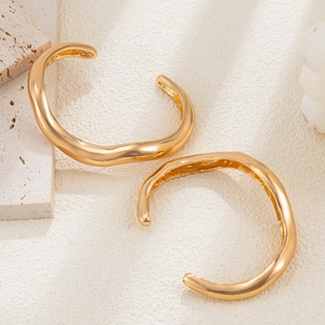 Detail van minimalistische gouden golvende armbanden op een travertijnse ondergrond