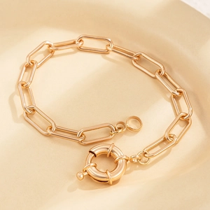 Macro detail of a minimalist gold paperclip chain bracelet with a large sailor clasp