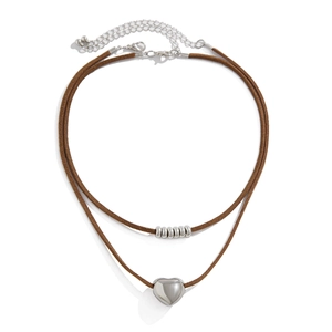 Detail van een dubbellaagse choker met zilveren hartvormige hanger en metalen ringaccenten
