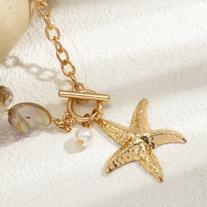 Detailed close-up of golden starfish pendant with pearl and shell charm on OT clasp chain