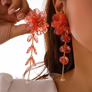 Détail de boucles d'oreilles à fleurs rouges avec pétales en résine et chaînes dorées