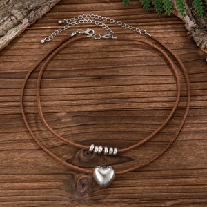 Detail van dubbellaagse ketting met hartjeshanger op bruin koord en houten achtergrond