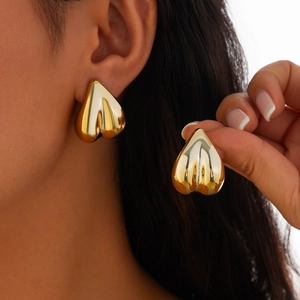 Gros plan de boucles d'oreilles cœur dorées avec finition miroir poli sur le modèle