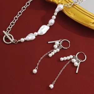 Détail du collier chaîne argenté et boucles d'oreilles perles sur fond de tissu rouge