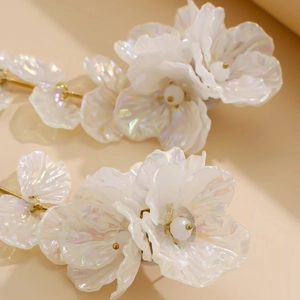 Gros plan de boucles d'oreilles fleurs irisées avec détails dorés et perle centrale