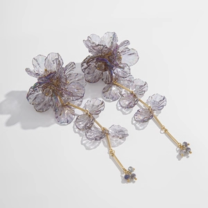 Vue macro de boucles d'oreilles fleurs en résine irisées violettes avec longs glands dorés