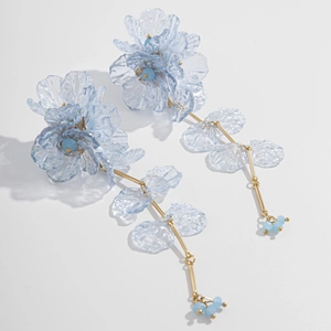 Détail des boucles d'oreilles fleurs translucides bleu clair avec glands dorés