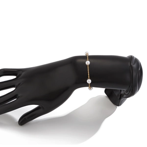 Détail d'un bracelet élégant en chaîne dorée avec quatre perles blanches sur support noir