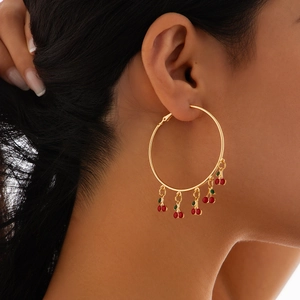 Close-up of gold hoop earrings with red cherry pendants and green leaves on model