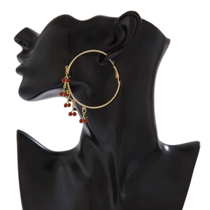 Close-up of gold hoop earrings with red cherry pendants on a black mannequin