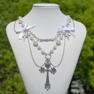 Dettaglio della collana a croce gotica con perle finte e fiocco di seta su un busto