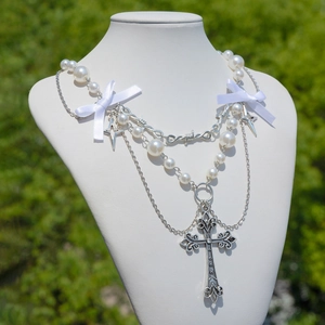 Dettaglio del ciondolo a croce e fiocco in nastro su collana multistrato di perle