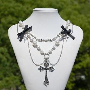 Dettaglio di collana gotica con croce, fiocchi neri e perle su un busto bianco