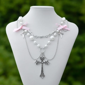 Dettaglio collana a strati con croce, perle finte e fiocco rosa su busto da esposizione